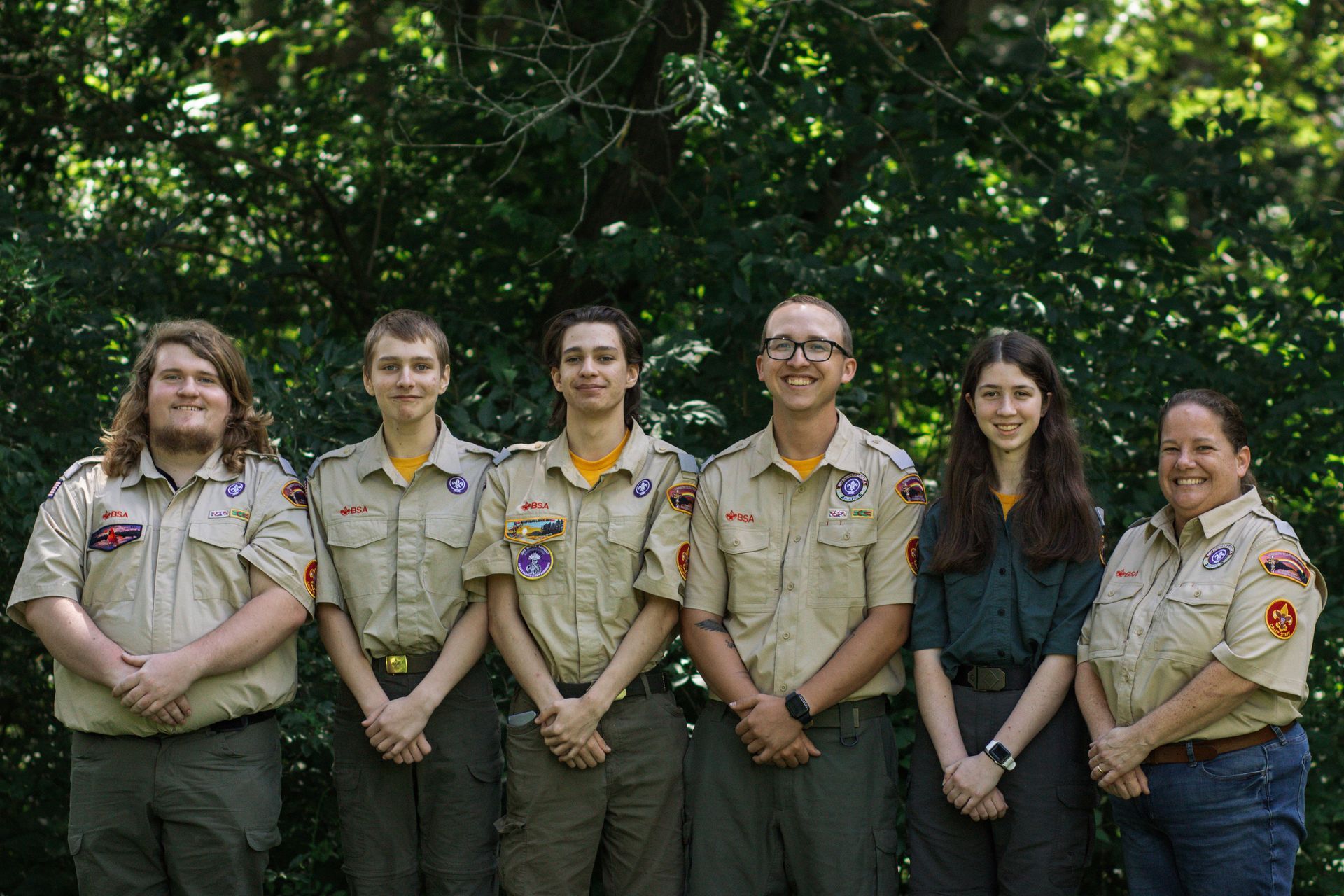 A group of boy scouts are posing for a picture in front of trees.