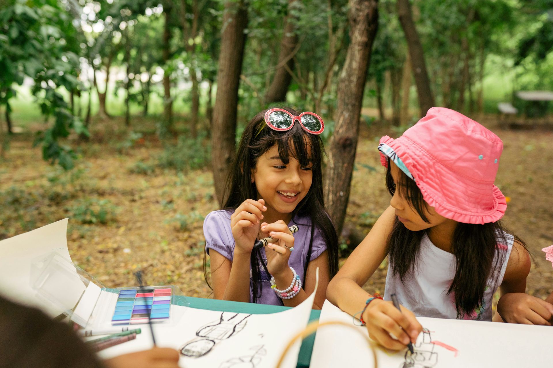 Two young girls are sitting at a table in the woods.