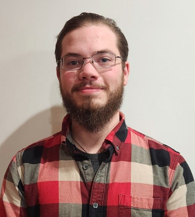 A man with a beard and glasses is wearing a plaid shirt.