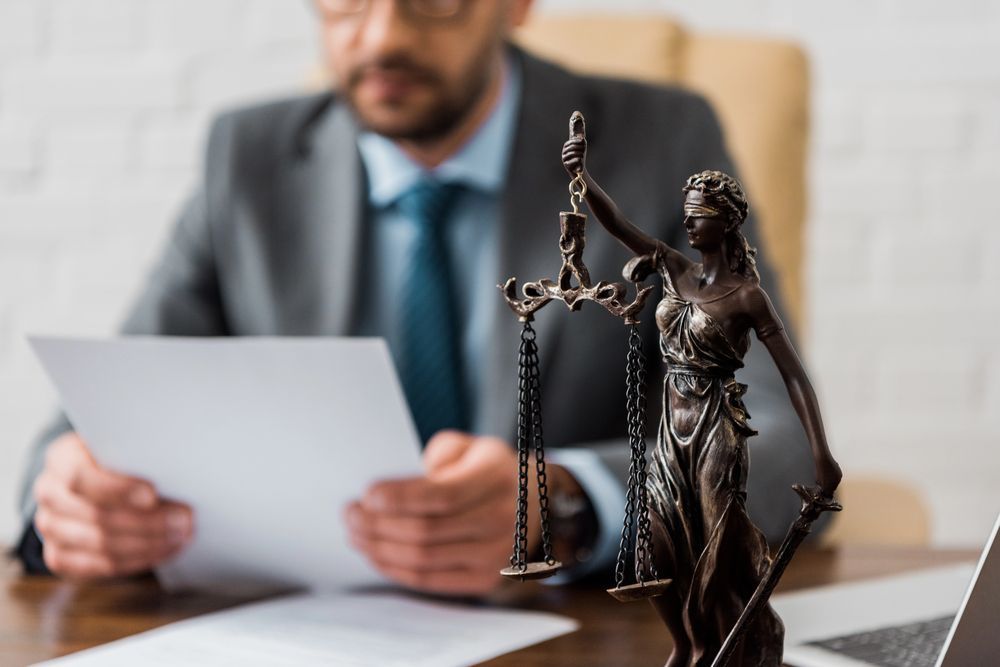 Un hombre con traje y corbata está sentado en un escritorio con una estatua de la justicia.