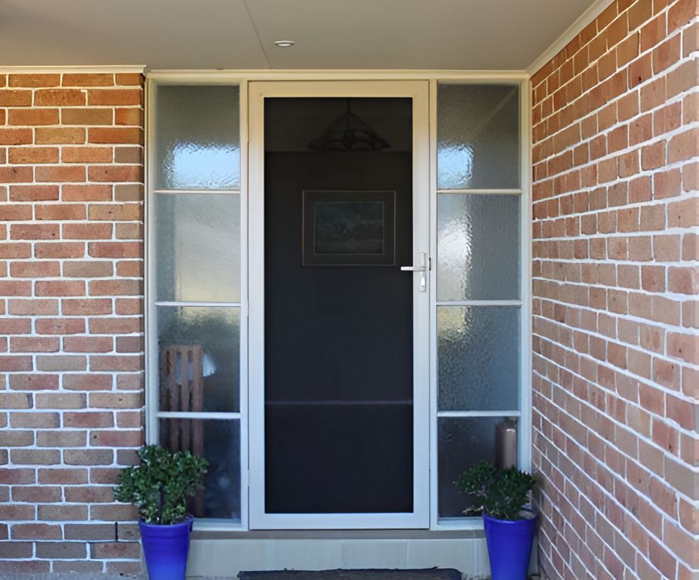 A Brick Wall With A White Door And Two Blue Potted Plants — All Hours Glass In Culburra Beach, NSW