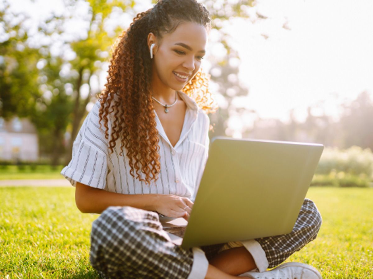 A woman is sitting on the grass using a laptop computer.