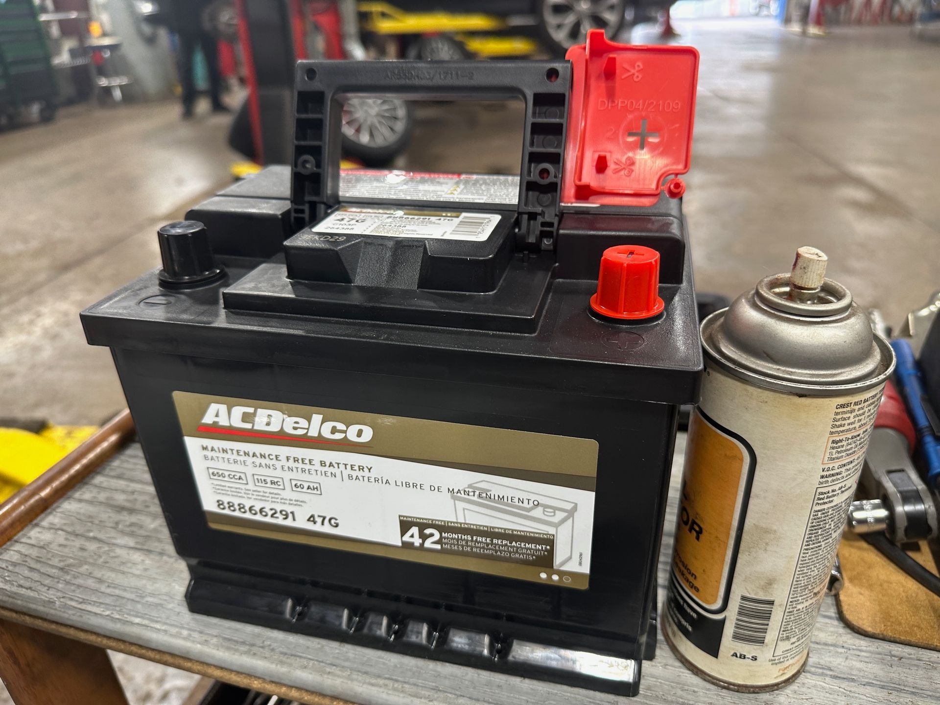 An acdelco battery is sitting on a wooden table next to a spray can. | Lou's Car Care Center, Inc.