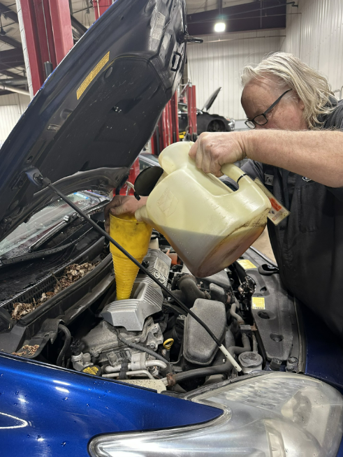 Auto Technician adding oil to an engine in a blue car. Lou's Car Care Center, Inc.
