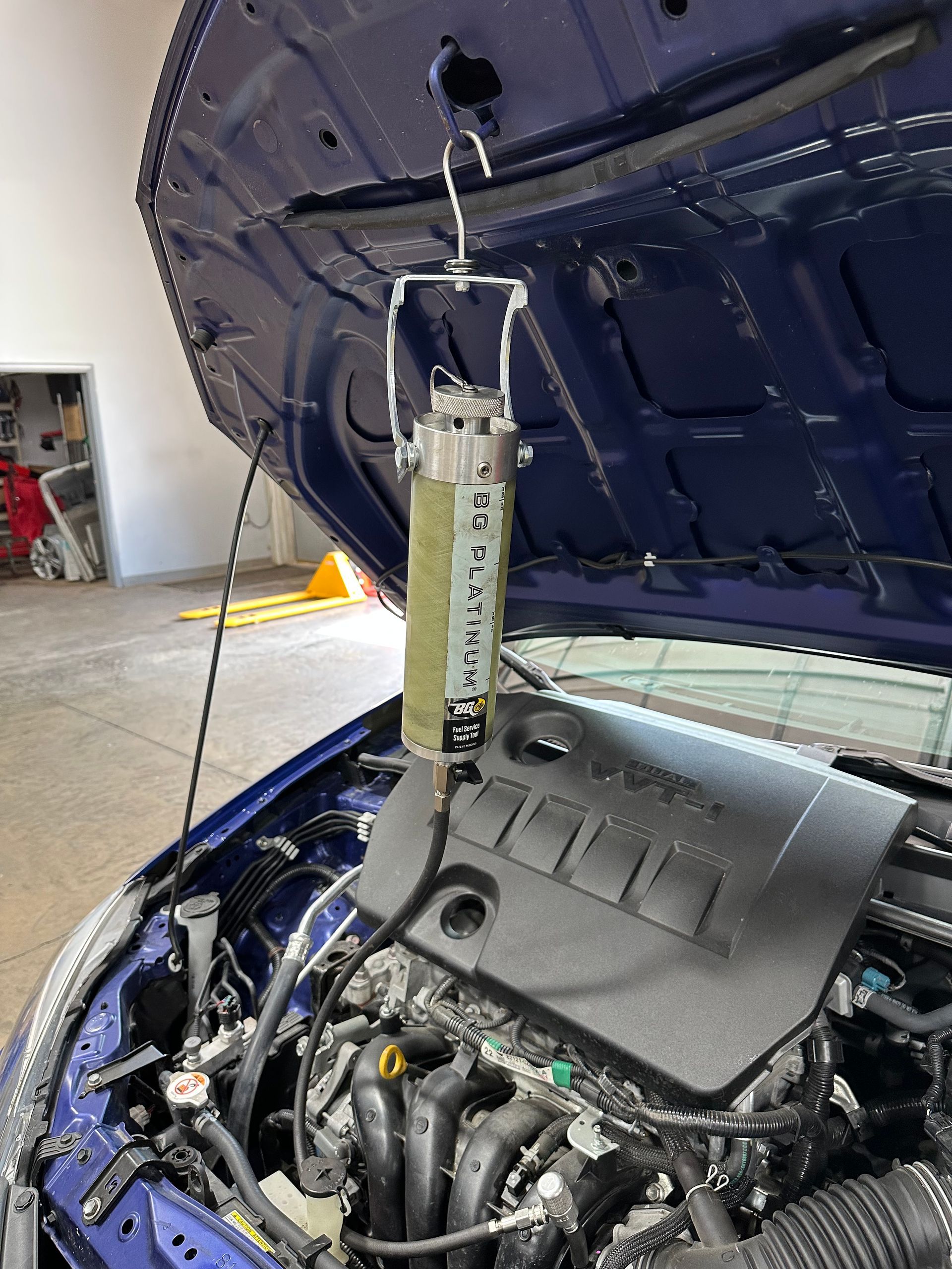 A BG Fuel System tool hanging from hood of a blue vehicle during fuel service. | Lou's Car Care Center