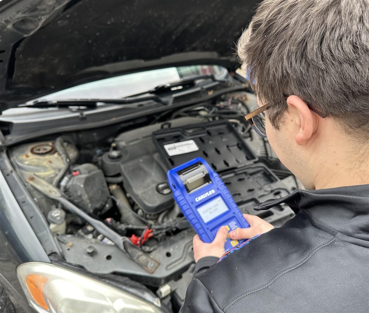 A man is looking under the hood of a car | Lou's Car Care Center, Inc.