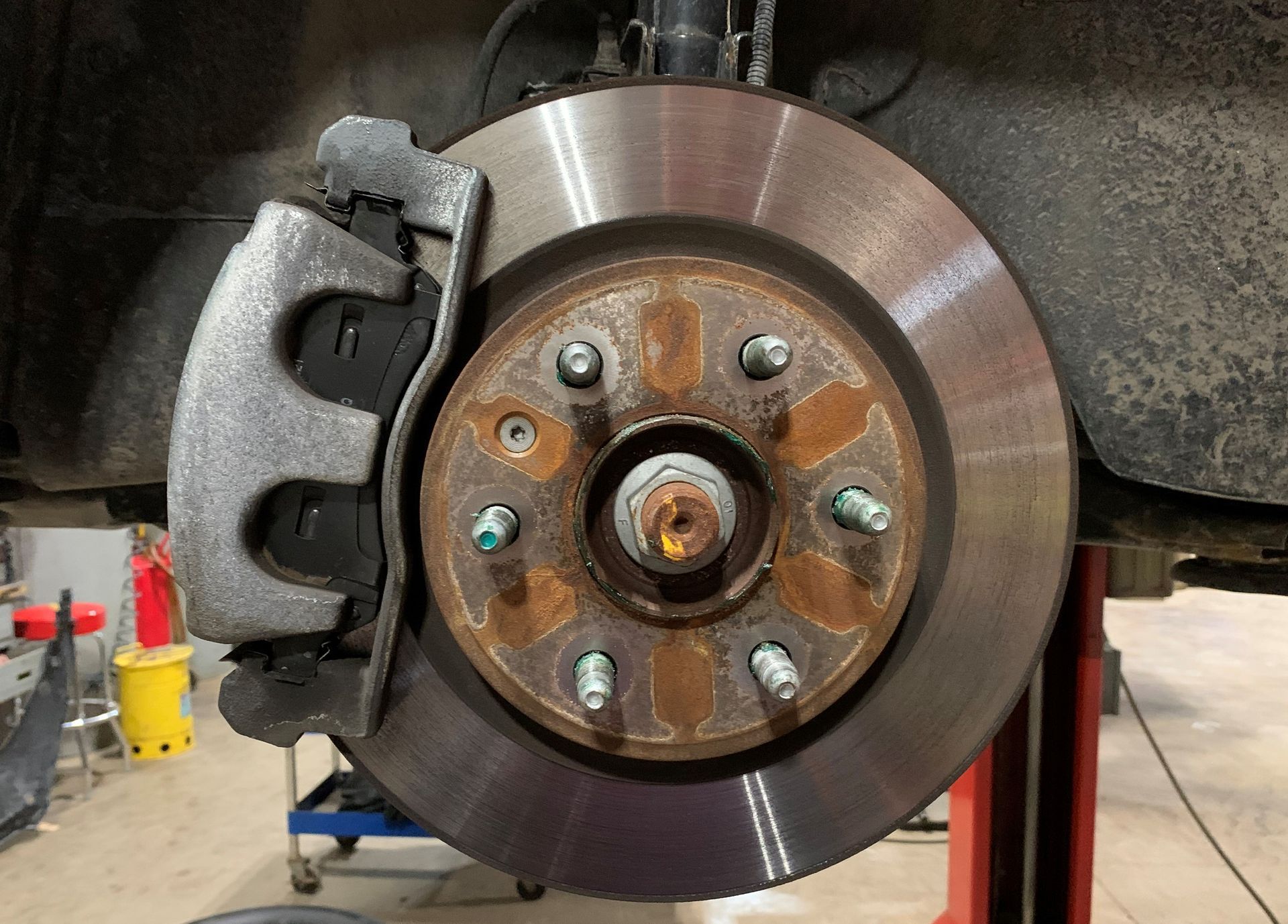 A close up of a brake disc on a car on a lift. | Lou's Car Care Center