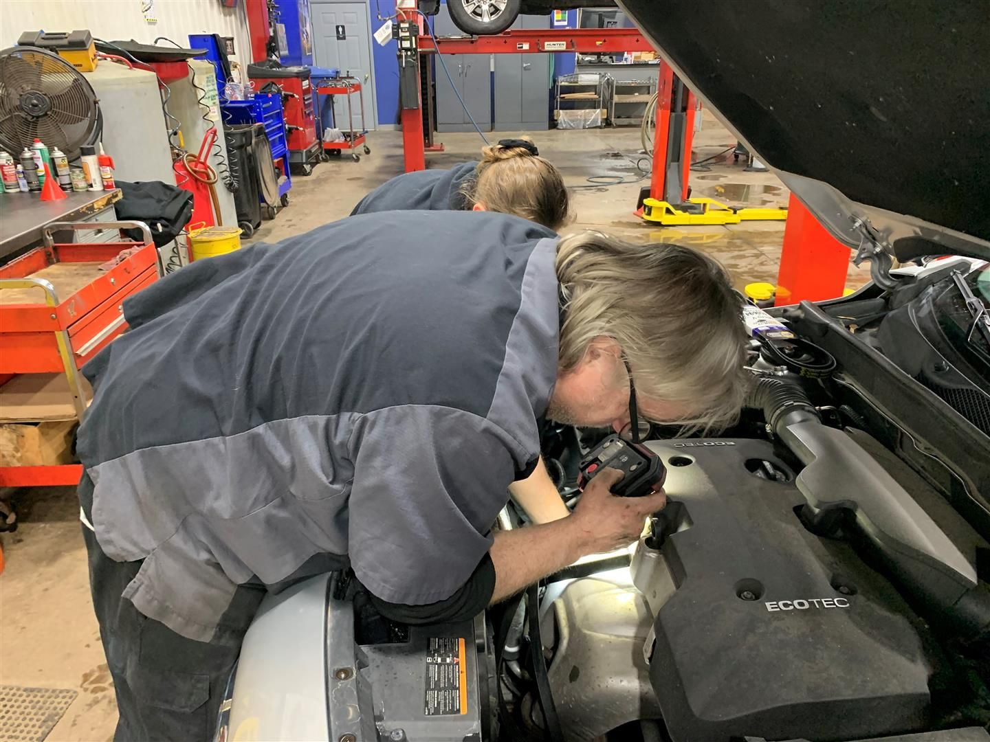 Two men are working under the hood of a car in a garage. | Lou's Car Care Center Inc.