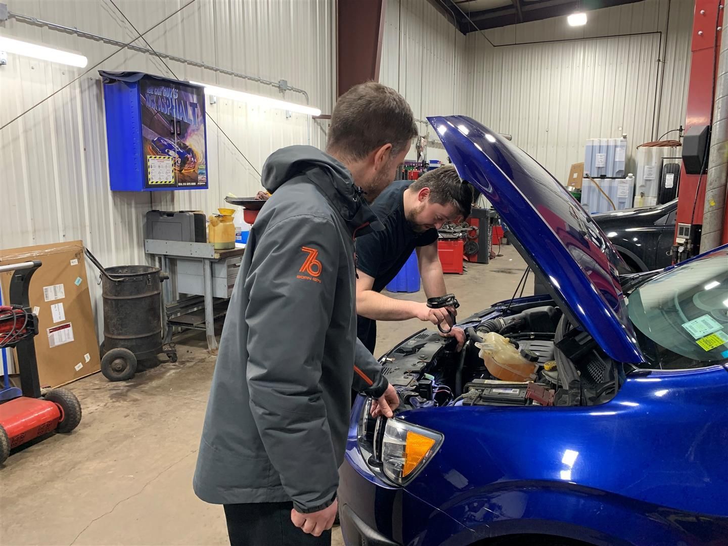 Two men are working on a blue car in a garage. | Lou's Car Care Center Inc.