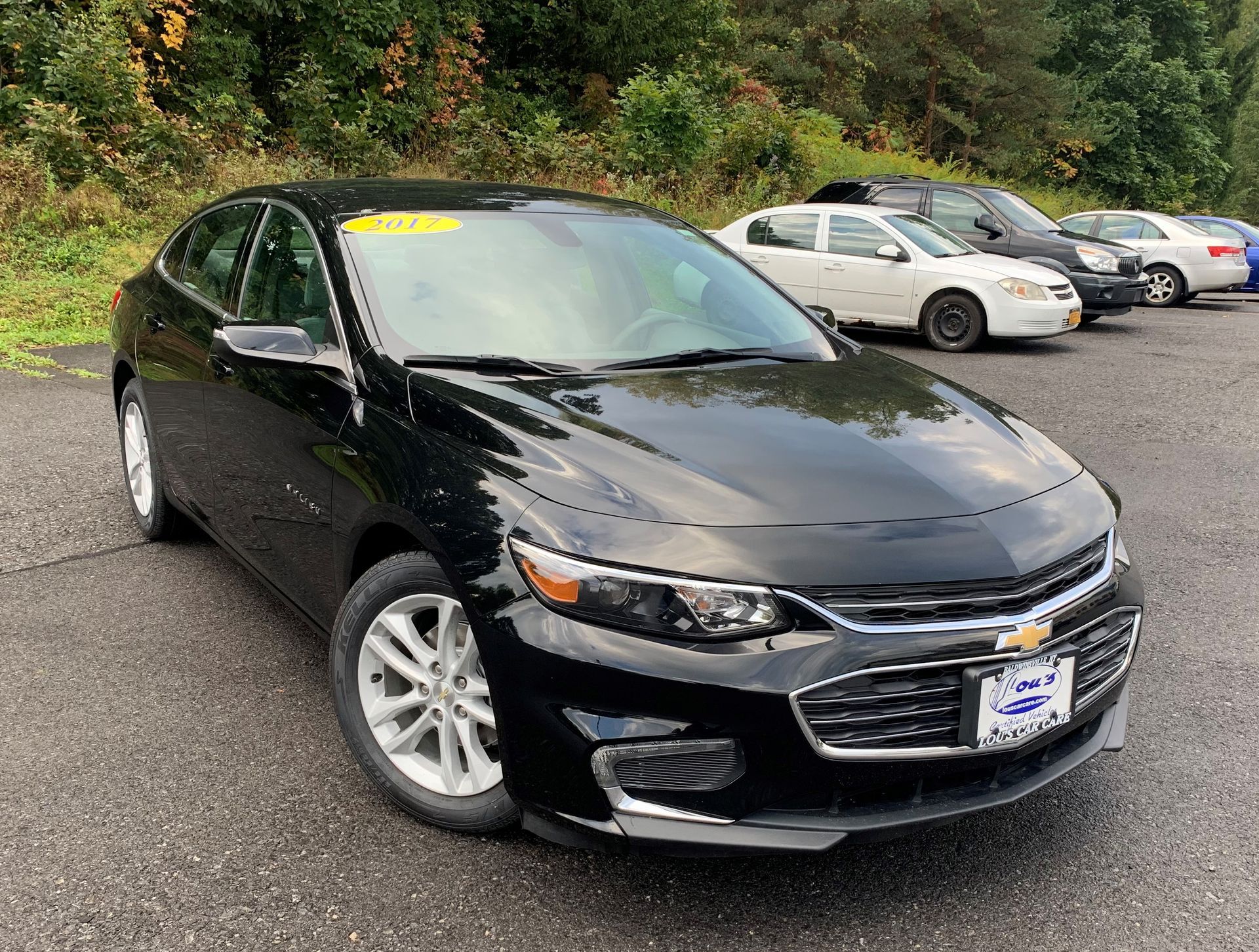 A black chevrolet malibu is parked in a lot with other cars.  | Lou's Car Care Center Inc.