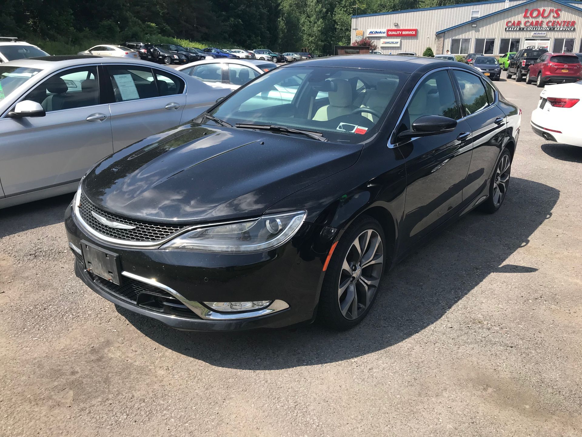 A black chrysler 200 is parked in a lot in front of a car dealership. | Lou's Car Care Center, Inc.