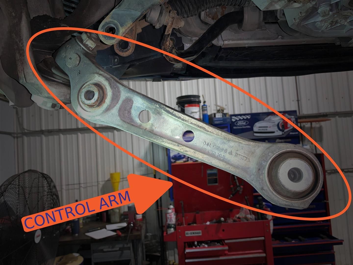 A control arm is shown under a car in a garage. | Lou's Car Care Center, Inc.