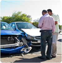 Two men are standing next to a car that has been damaged in an accident. | Lou's Car Care Center