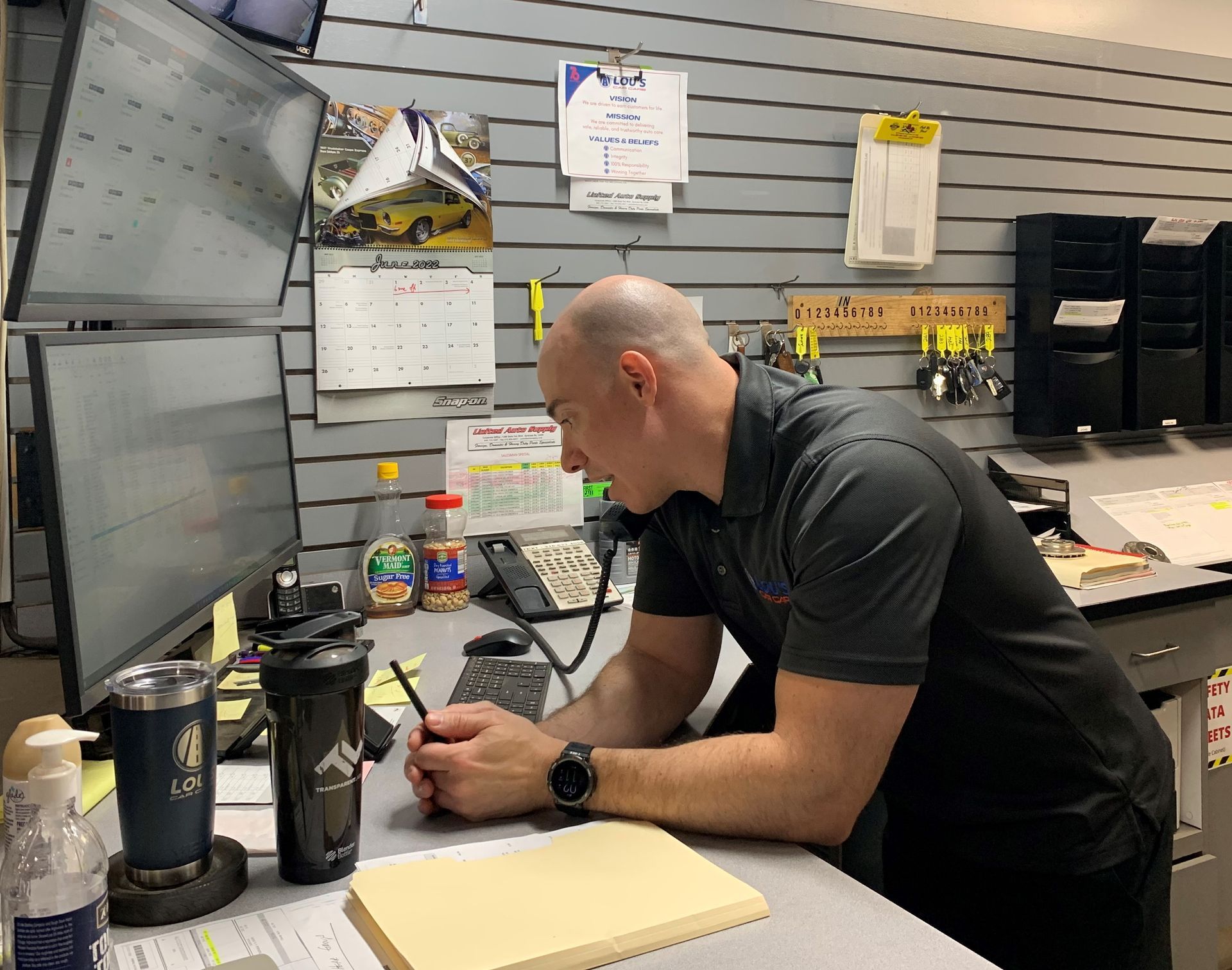 A man is sitting at a desk in front of a computer. | Lou's Car Care Center Inc.