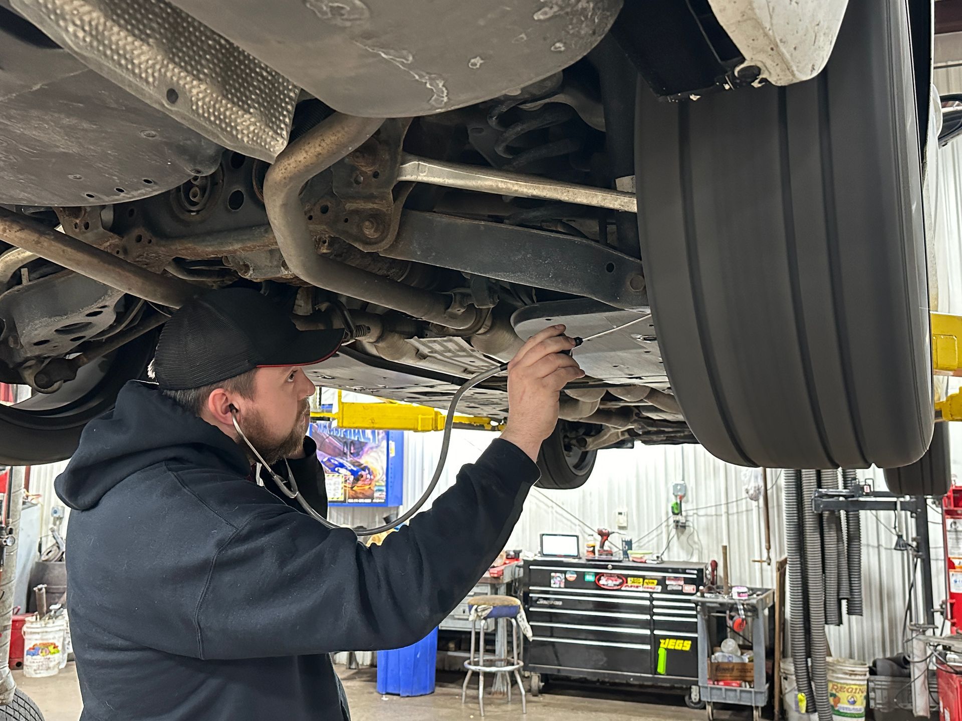 A man is working under a car in a garage. | Lou's Car Care Center, Inc.