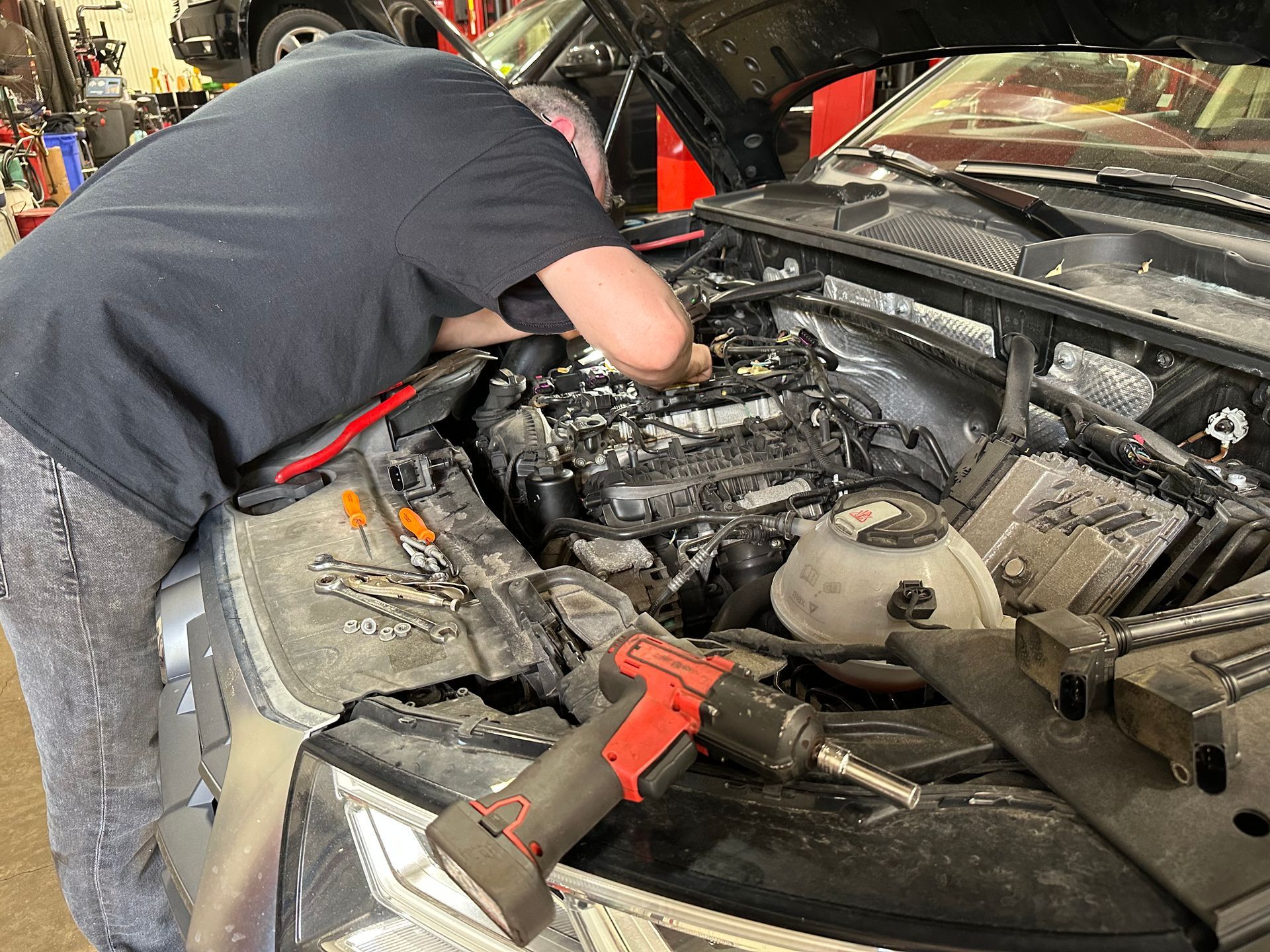 A man is working on the engine of a car in a garage. | Lou's Car Care Center, Inc.