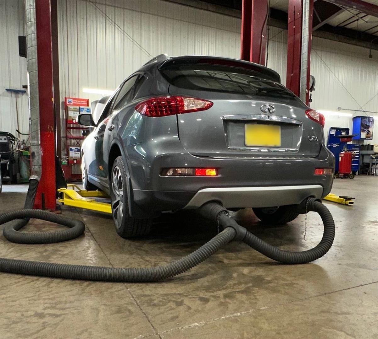 A gray car is sitting on a lift in a garage. | Lou's Car Care Center, Inc.