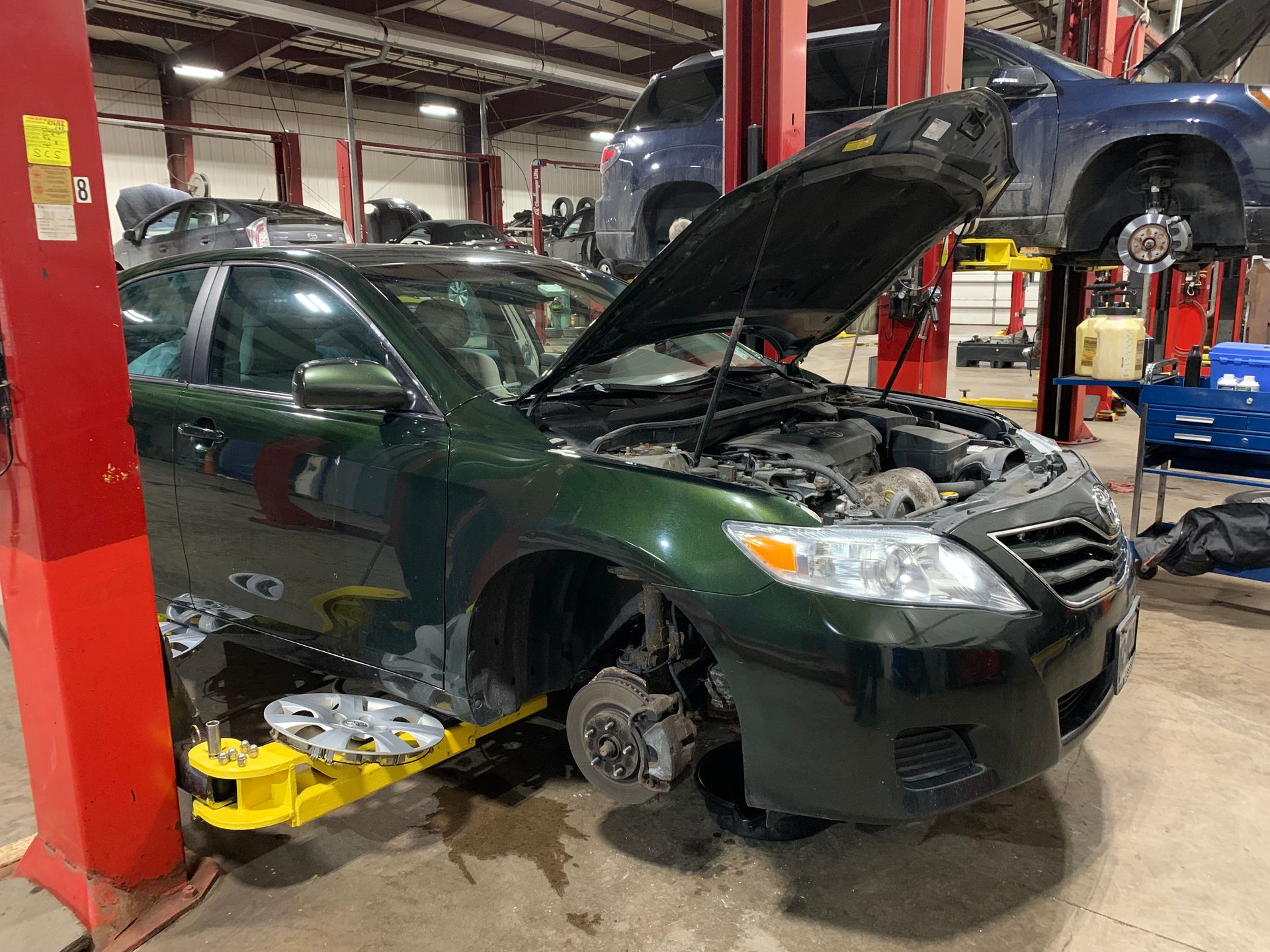 A green car with the hood up is on a lift in a garage. | Lou's Car Care Center, Inc.