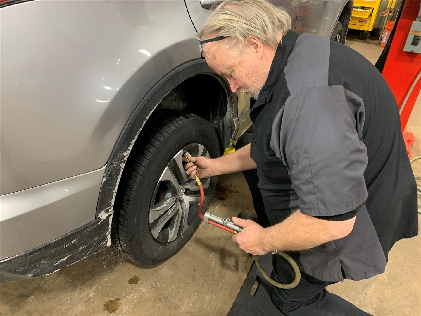 A man is inflating a tire with a hose in a garage. | Lou's Car Care Center Inc.