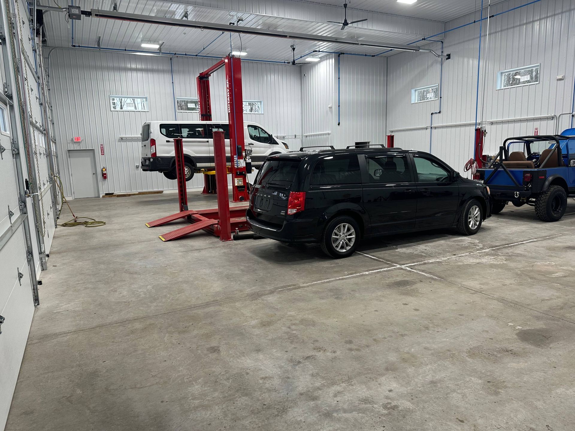White van, black van, and blue Jeep in medium duty truck shop with two, red lifts. | Lou's Car Care Center, Inc.