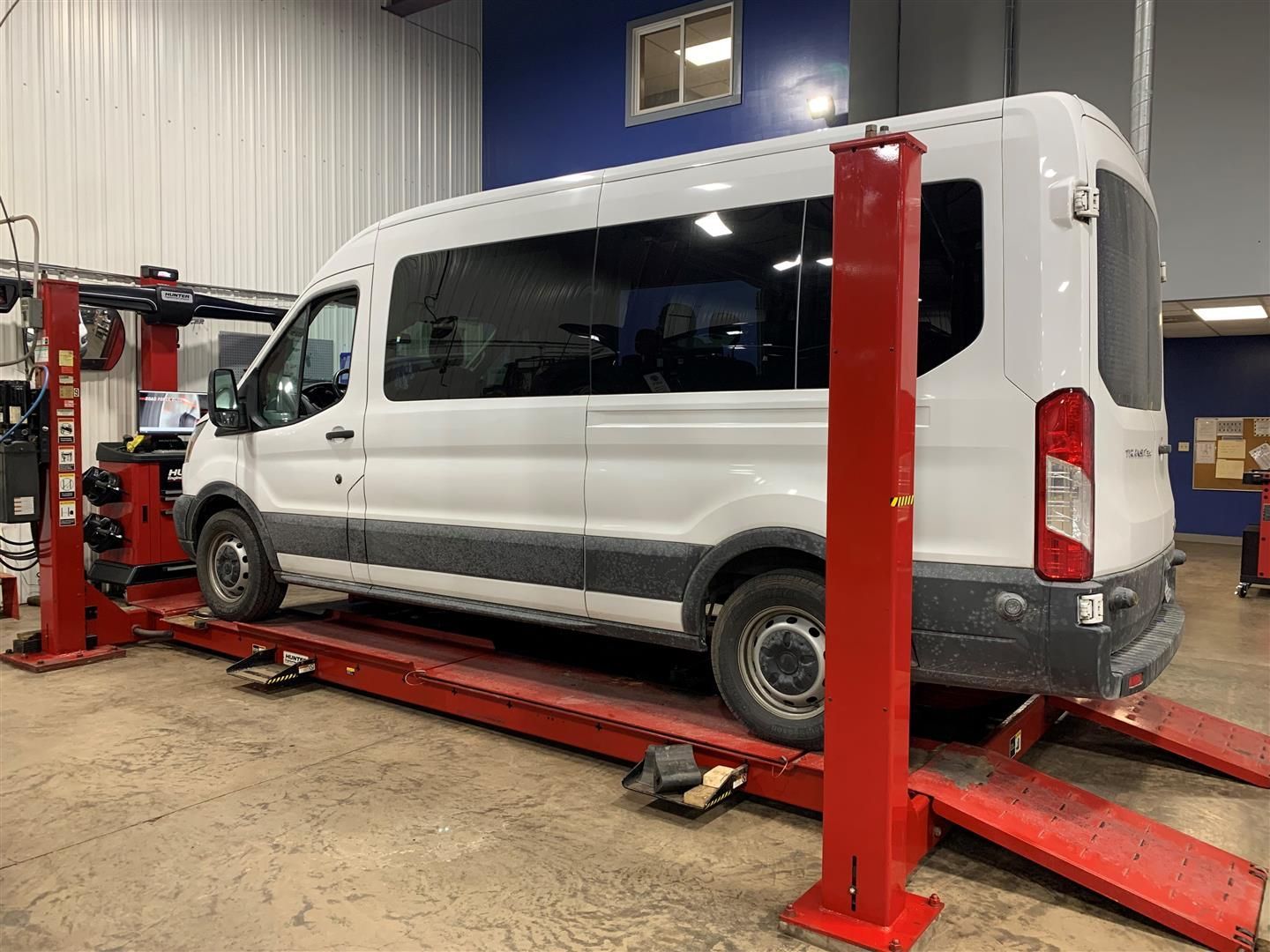 A white van is sitting on top of a red lift in a garage. | Lou's Car Care Center