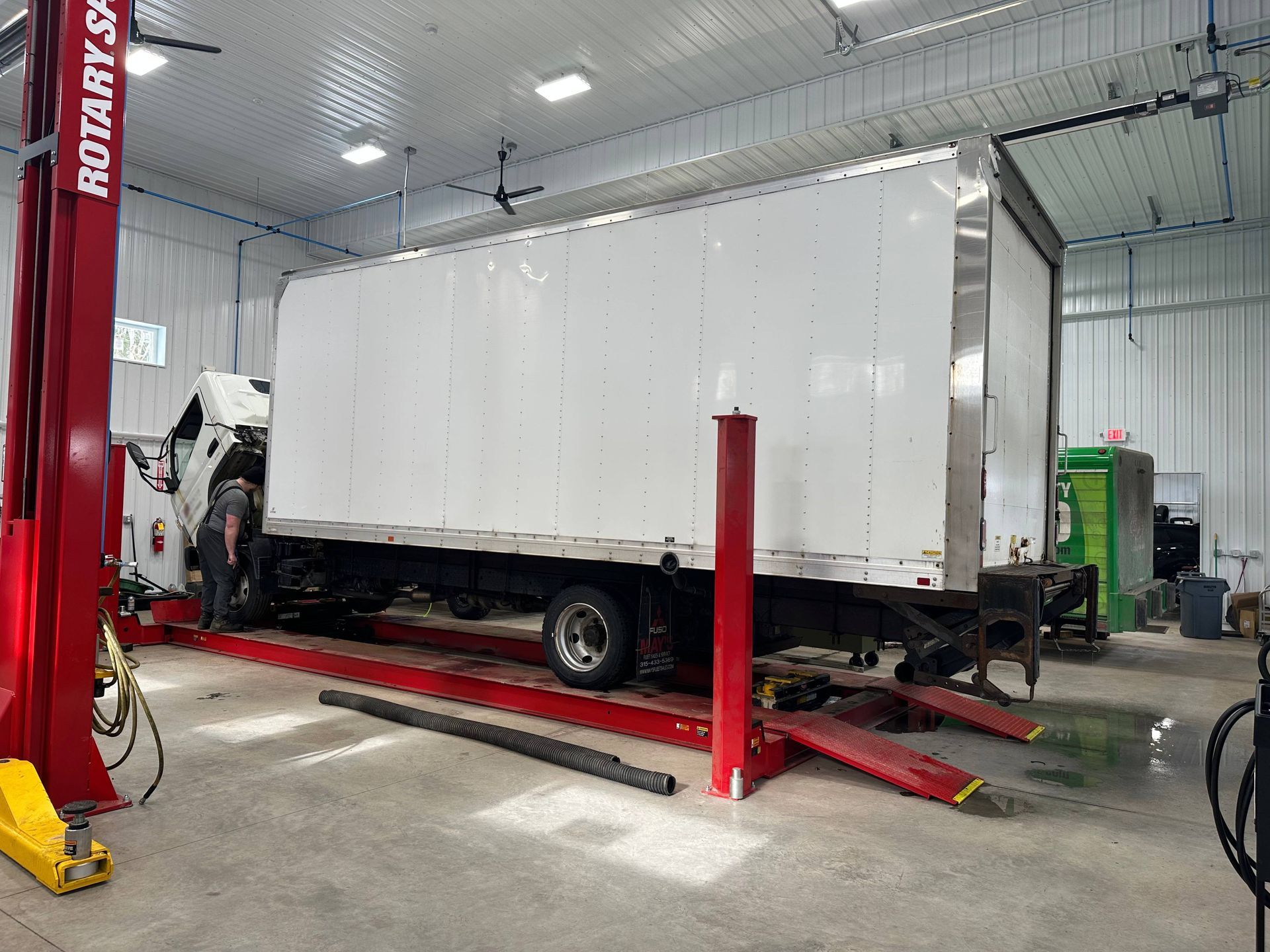 White box truck on red, vehicle rack with technician in gray clothing gives a visual inspection of the truck. | Lou's Car Care Center, Inc.