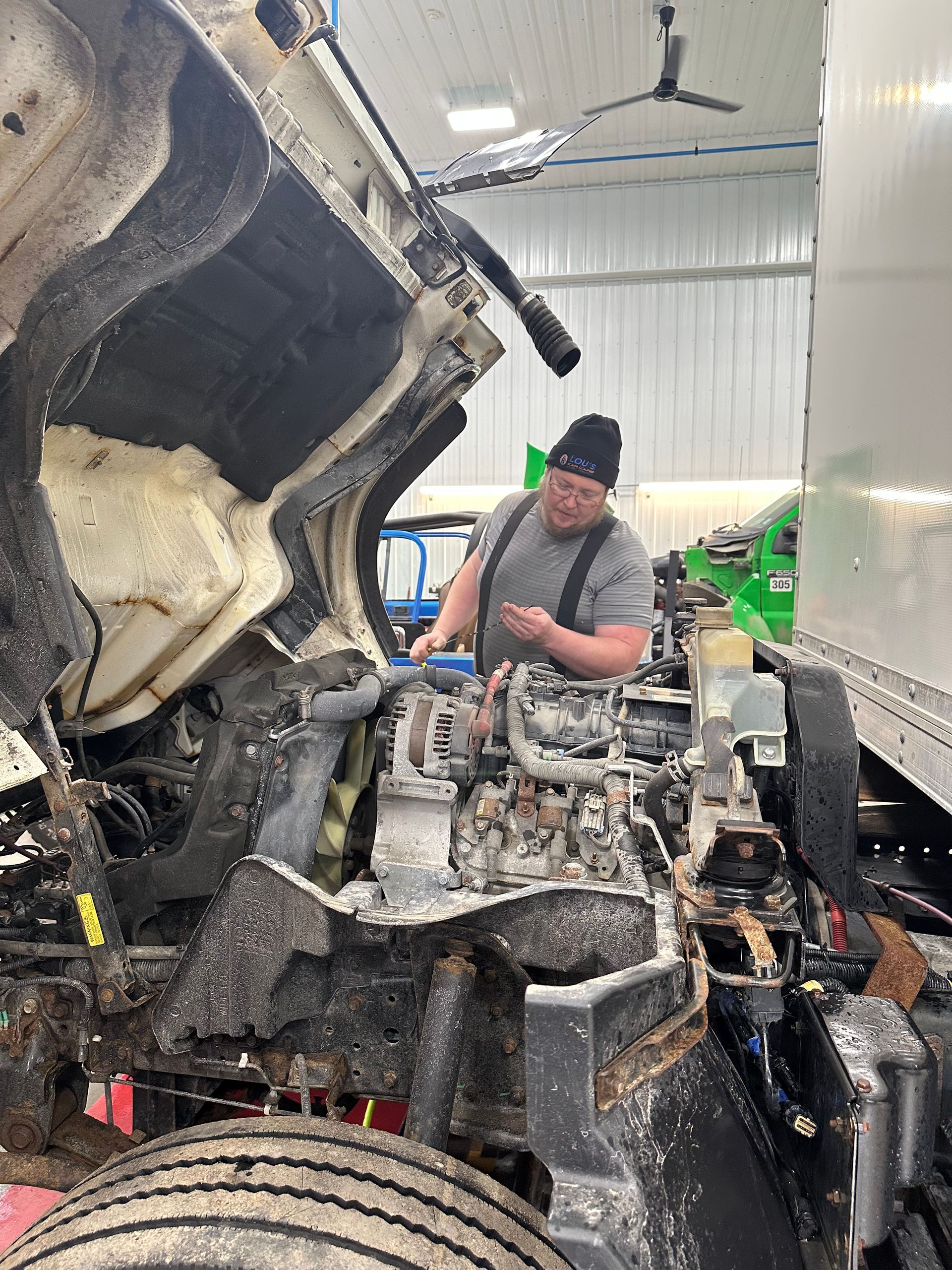 Auto technician checking oil level on white fleet truck in shop.| Lou's Car Care Center, Inc.