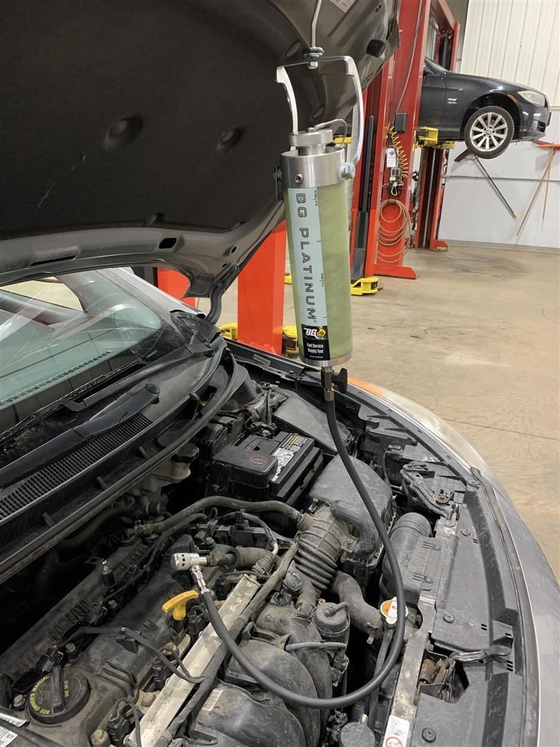 A car with the hood up is being worked on by a mechanic. | Lou's Car Care Center Inc.