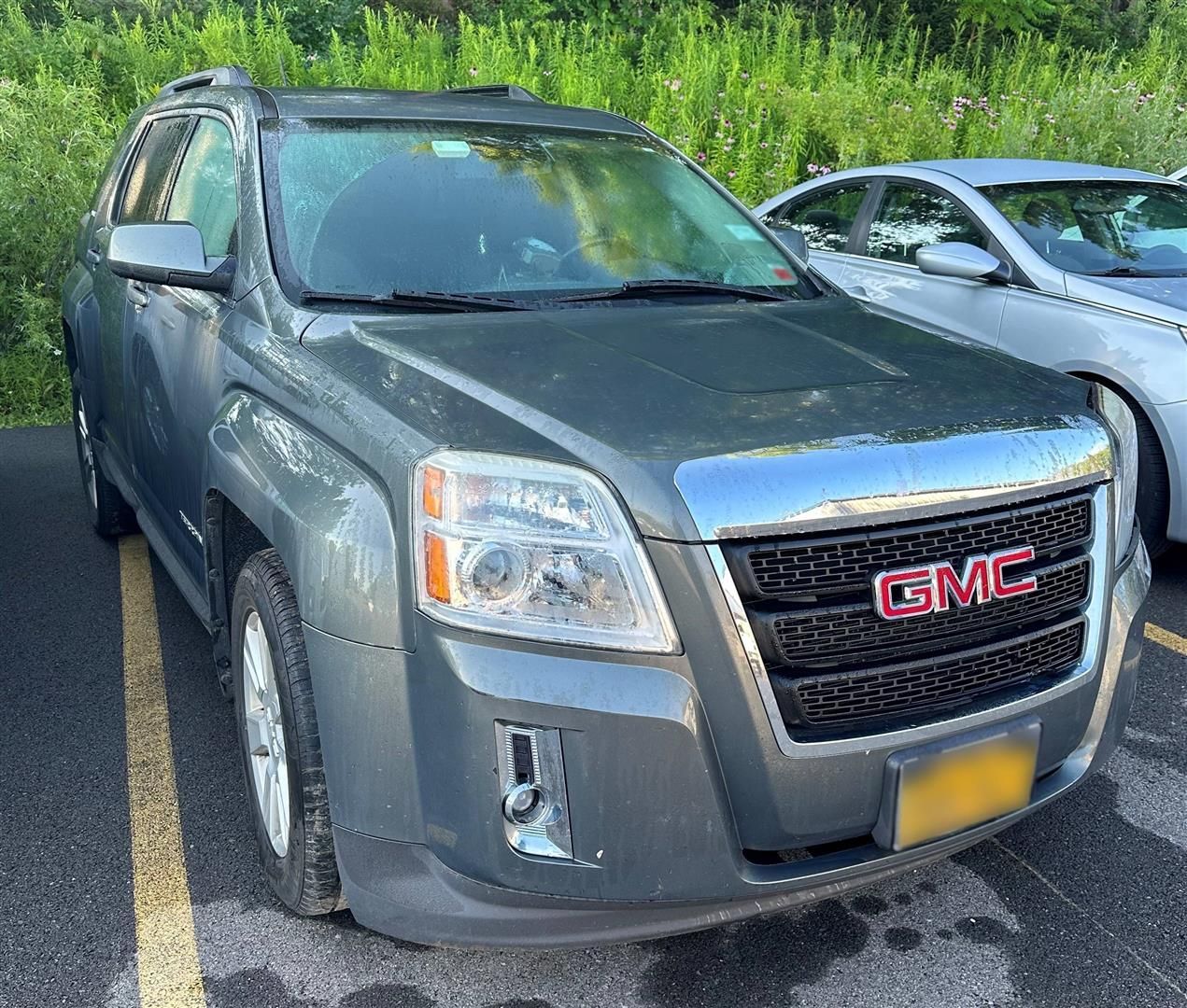 A gray gmc suv is parked in a parking lot next to a silver car. | Lou's Car Care Center, Inc.