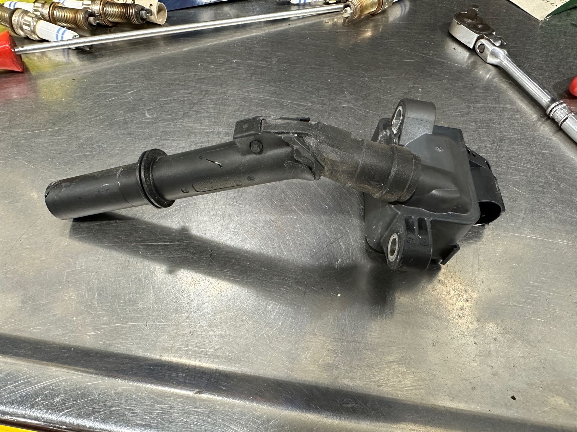 A broken ignition coil is sitting on a metal surface next to a wrench. | Lou's Car Care Center, Inc.