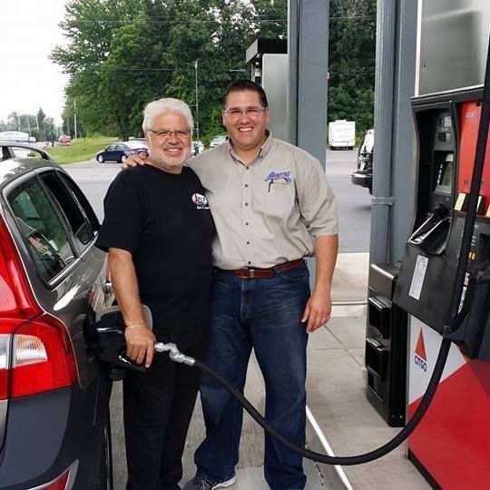 Two men are standing next to each other at a gas station | Lou's Car Care Center