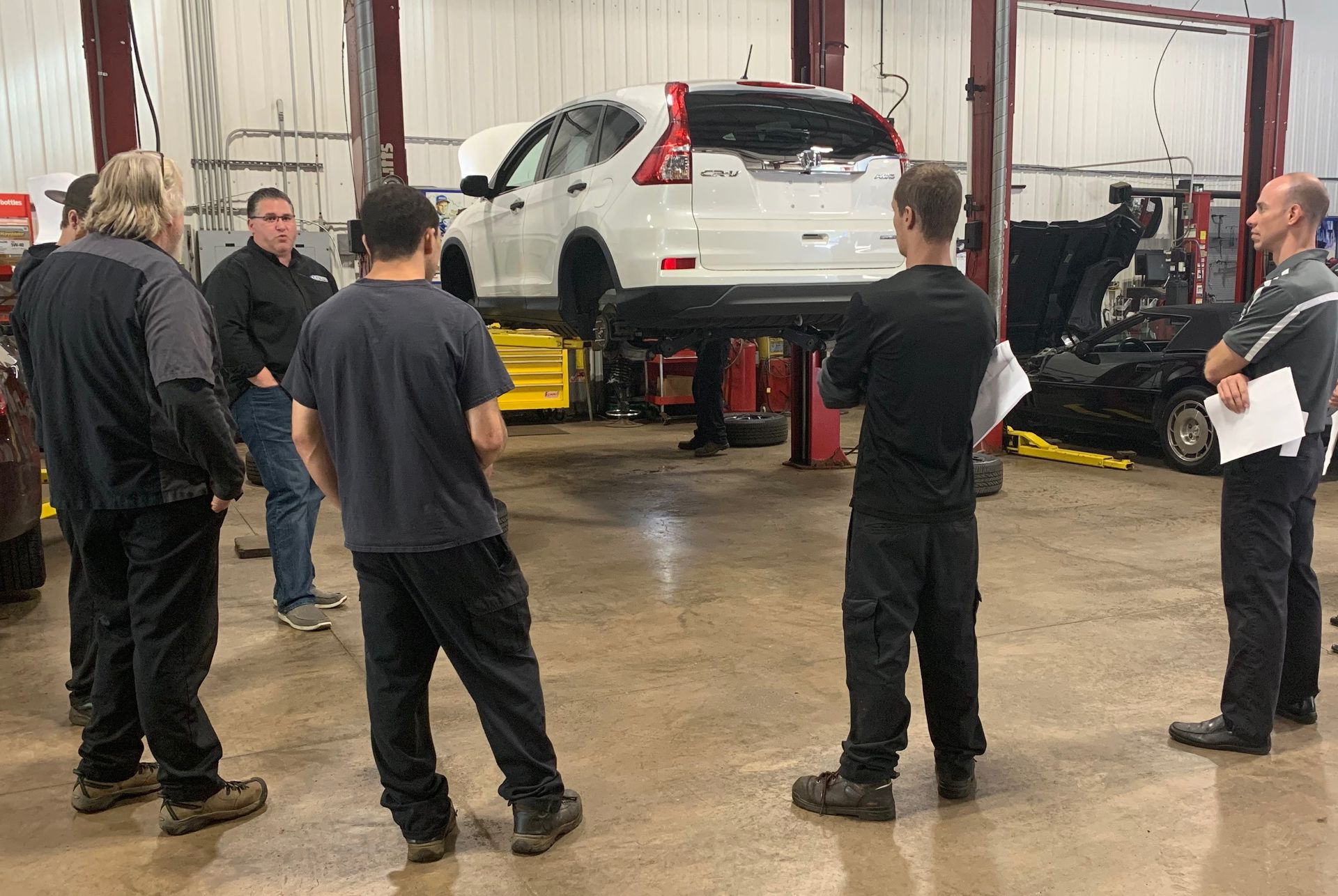 A group of men are standing around a car in a garage. | Lou's Car Care Center