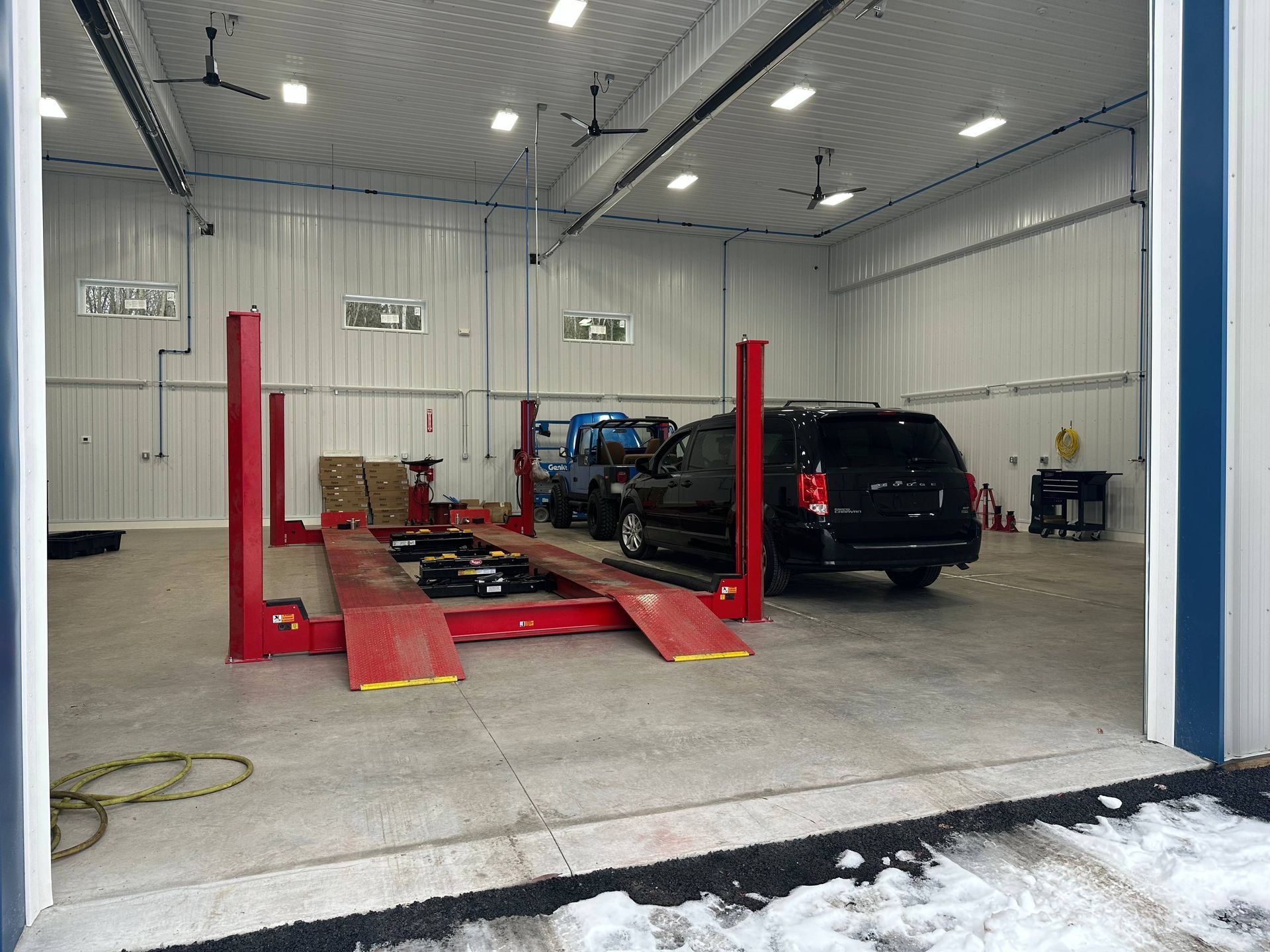 Red, medium duty truck lift in garage with a blue Jeep and black van to the right of it. | Lou's Car Care Center, Inc.