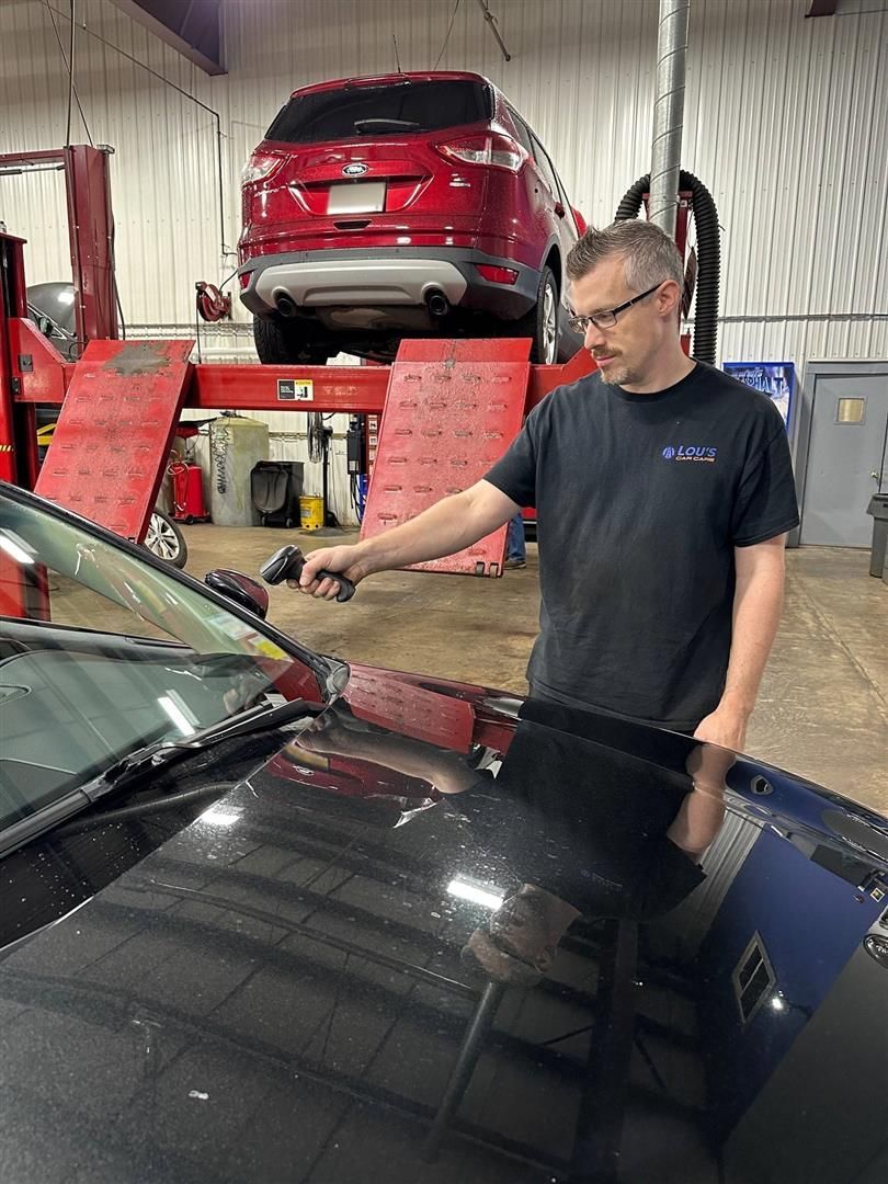 A man is cleaning the windshield of a car in a garage. | Lou's Car Care Center, Inc.