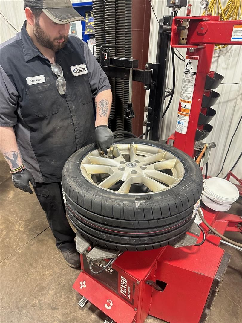 A man is changing a tire on a machine in a garage.  | Lou's Car Care Center, Inc.