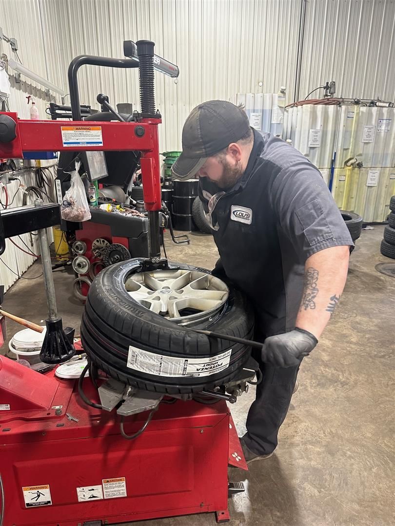 A man is changing a tire on a machine in a garage.  | Lou's Car Care Center, Inc.