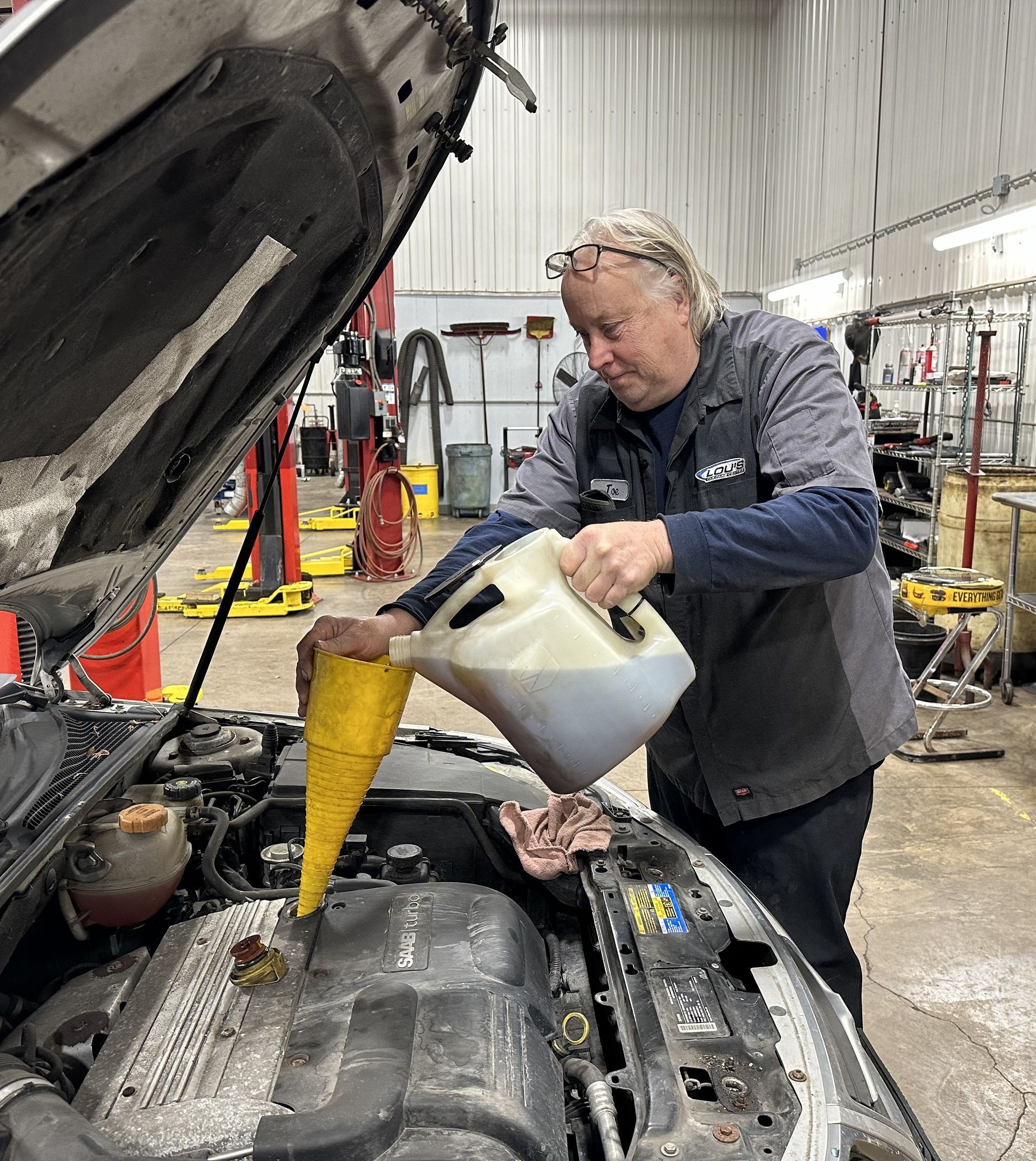 Auto technician filling engine with oil in the service bay. | Lou's Car Care Center