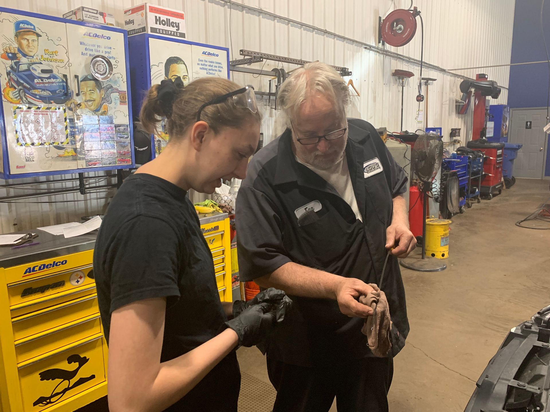 A man and a woman are working on a car in a garage. | Lou's Car Care Center, Inc.