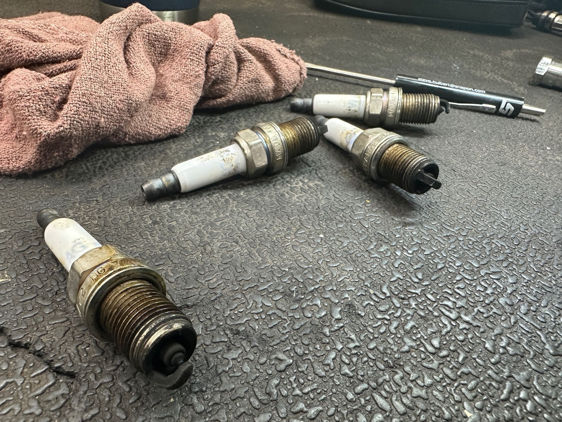 A bunch of spark plugs are sitting on a table next to a towel and a screwdriver. | Lou's Car Care Center, Inc.