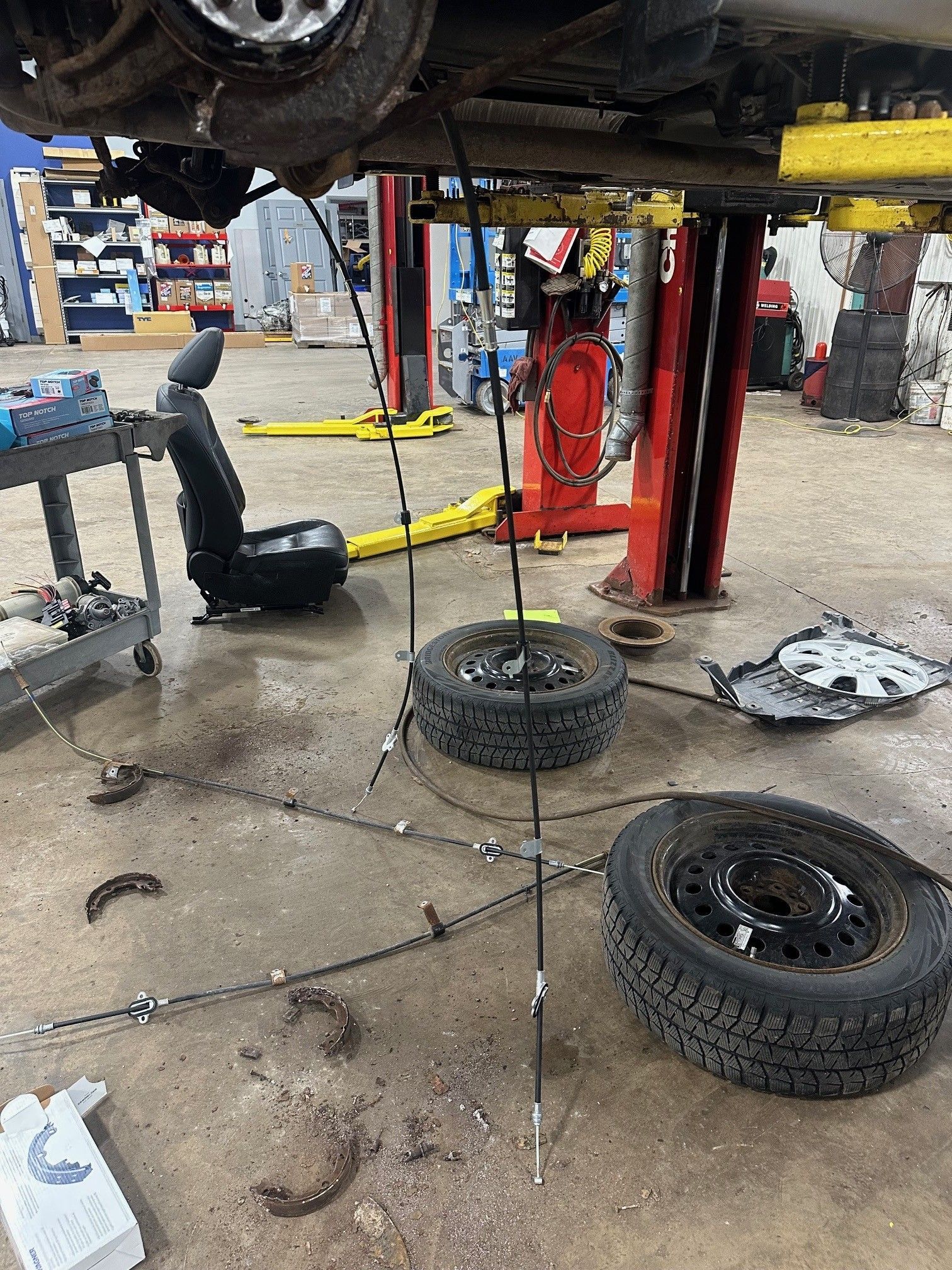 Parking brake cables hangning from vehicle on lift in the shop | Lou's Car Care Center, Inc.