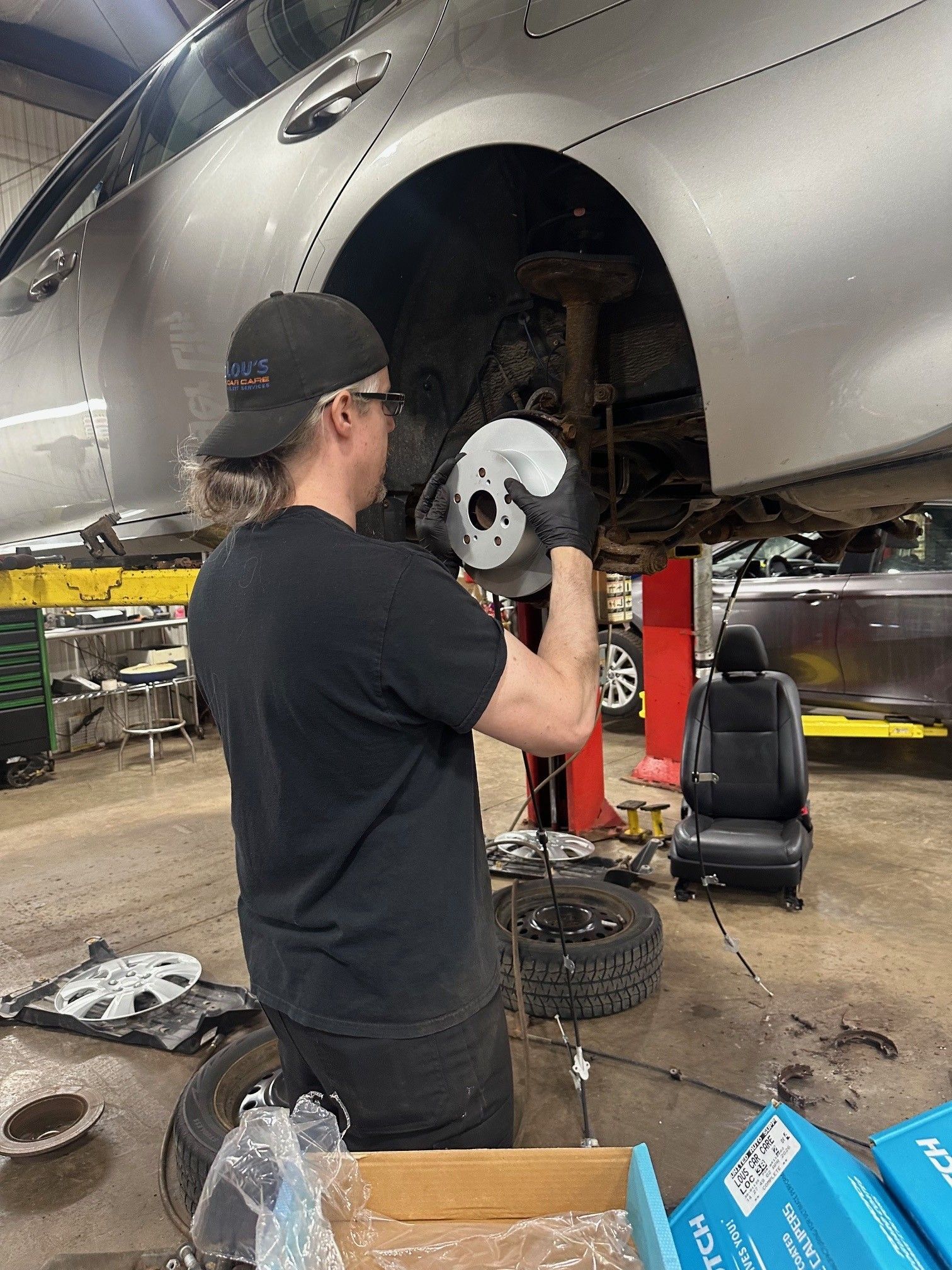 Auto Technician wearing black clothes installing new parkng brake shoes and brake rotors on a silver vehicle in the shop | Lou's Car Care Center, Inc.