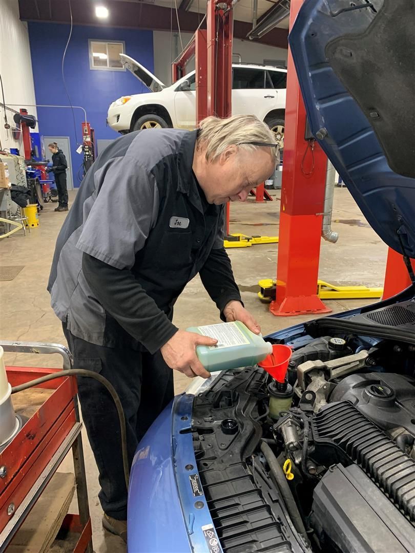 A man is looking under the hood of a car in a garage. | Lou's Car Care Center Inc.