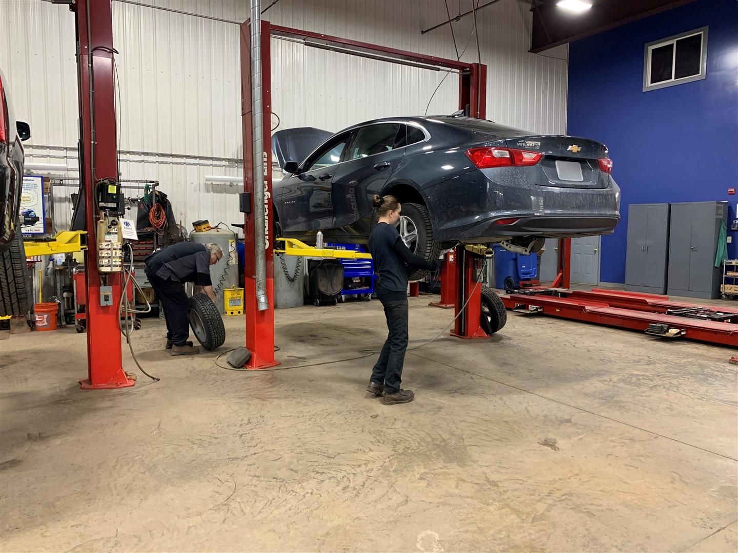 A man is working on a car on a lift in a garage.  | Lou's Car Care Center Inc.