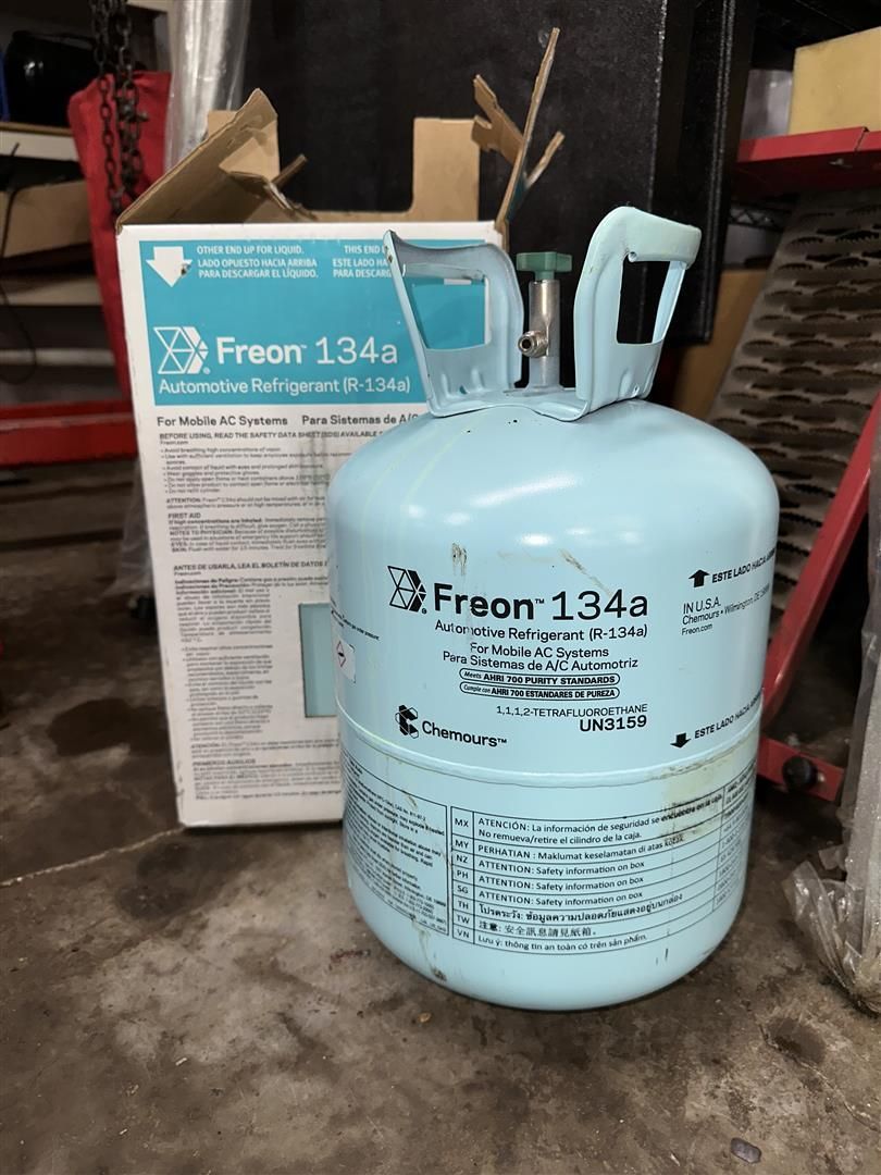 A cylinder of freon 134a is sitting next to a box | Lou's Car Care Center