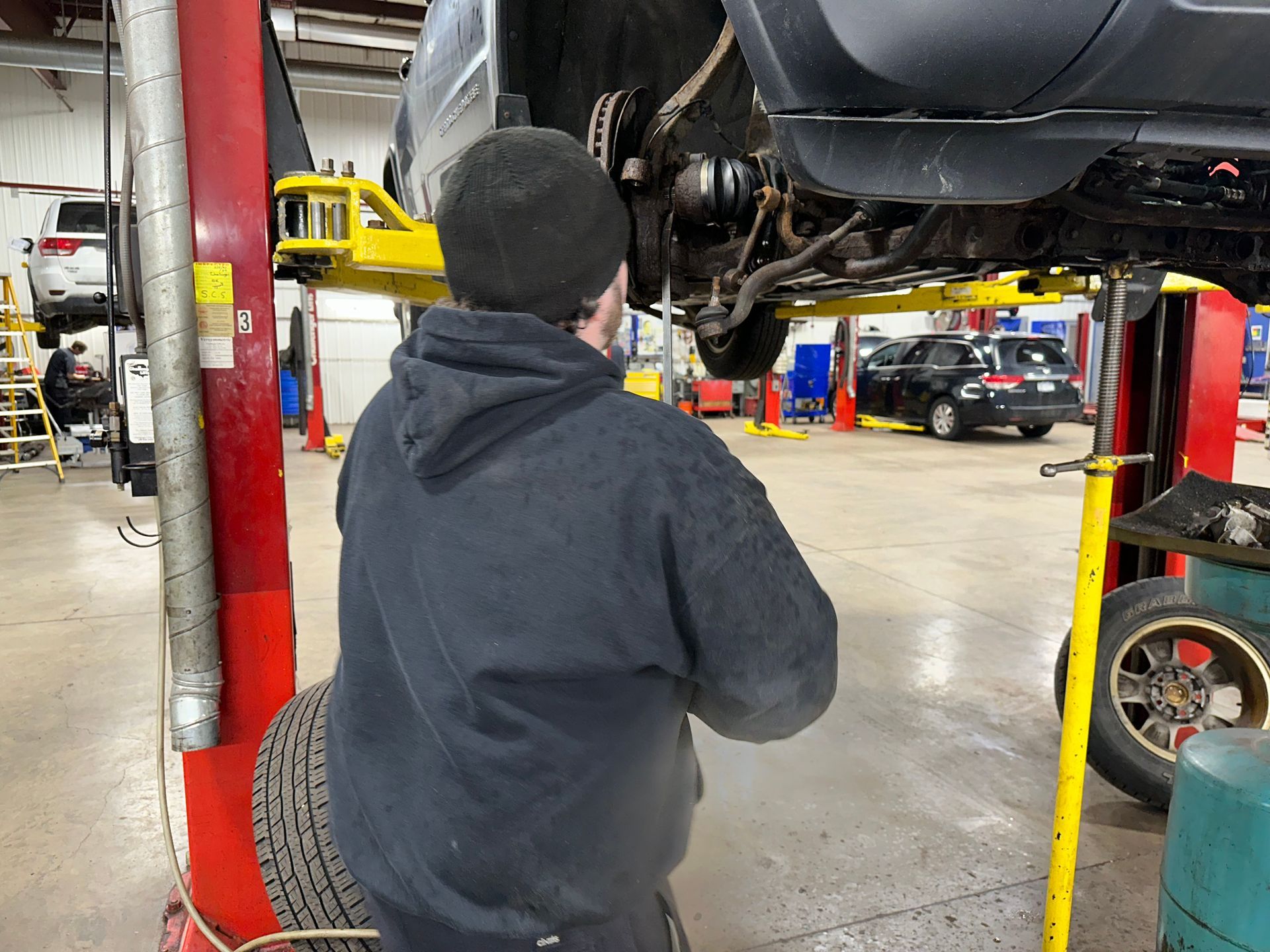 A man is standing under a car on a lift in a garage. | Lou's Car Care Center, Inc.