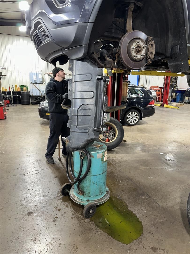 A man is working on a car on a lift in a garage. | Lou's Car Care Center, Inc.