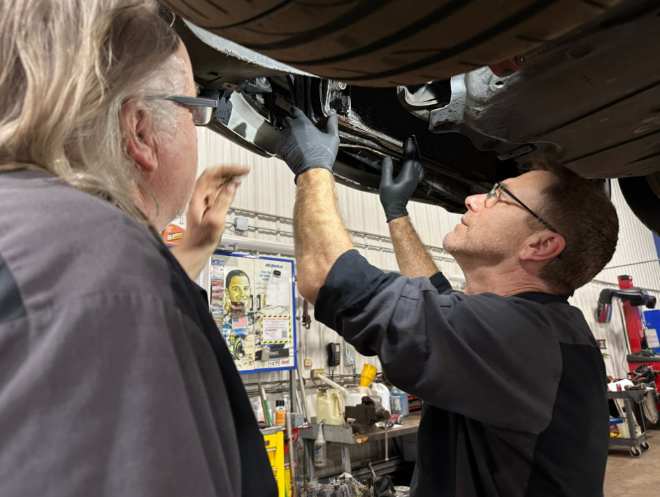 Two male technicians checking vehicle for a radiator leak in repair shop.