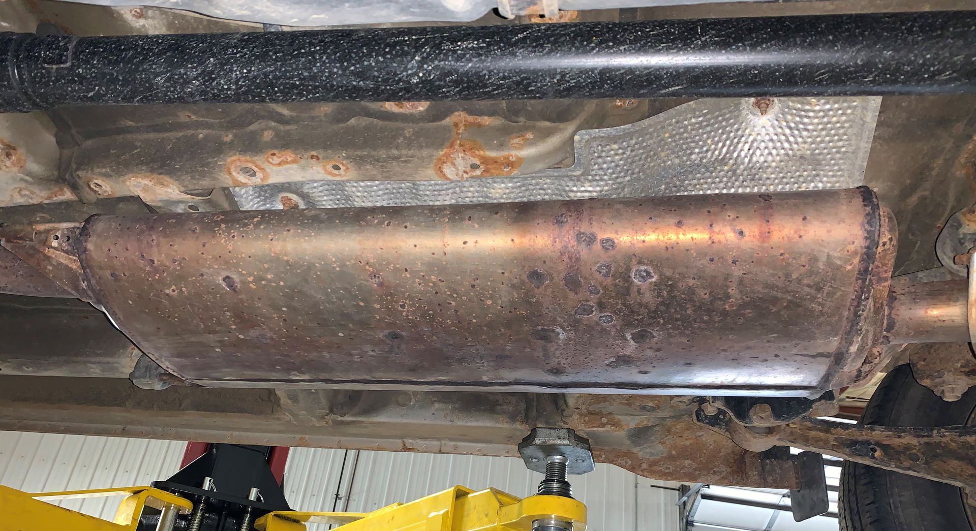 A rusty exhaust pipe is sitting underneath a car in a garage. | Lou's Car Care Center, Inc.