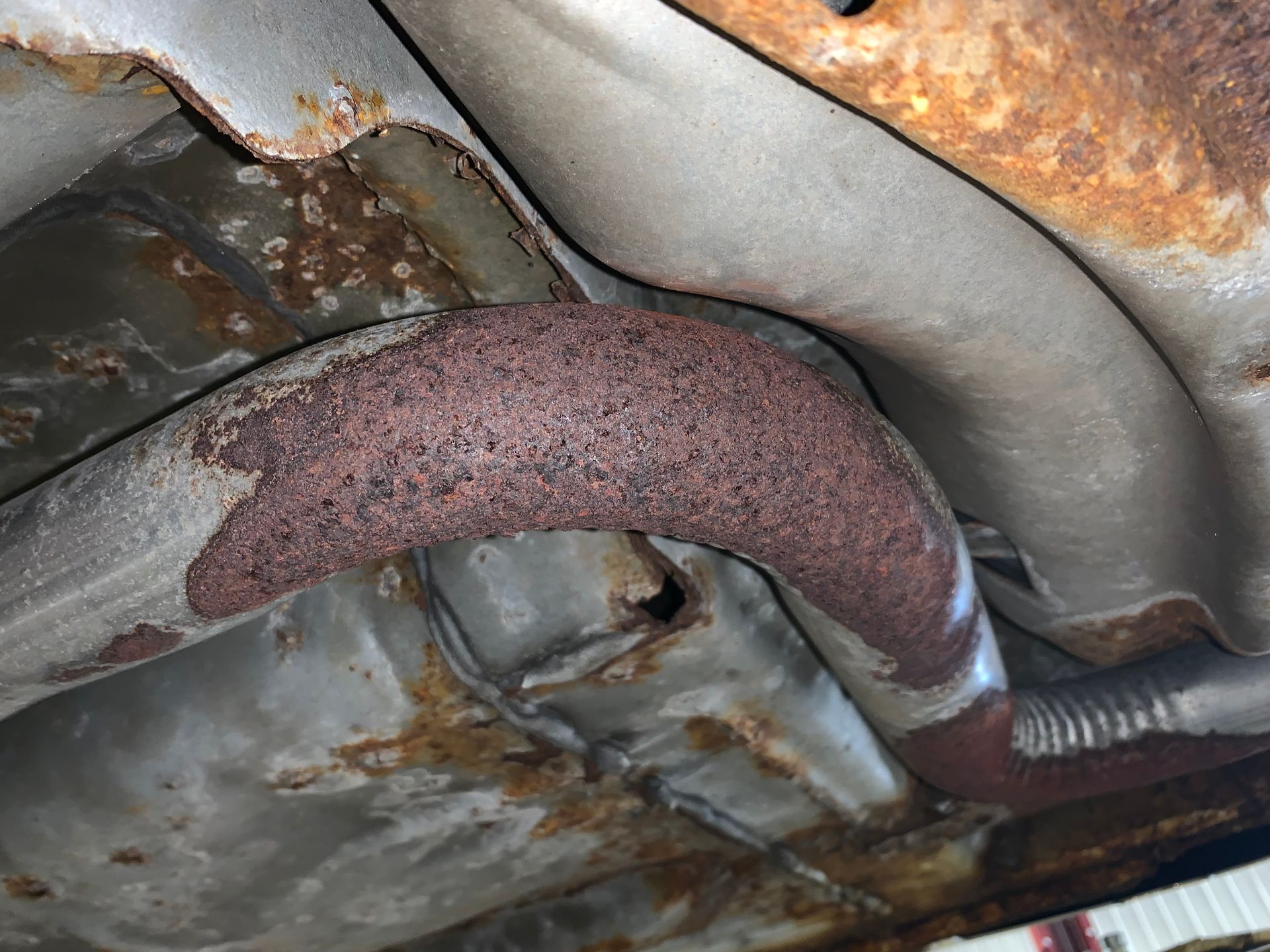 A close up of a rusty exhaust pipe on the underside of a car. | Lou's Car Care Center, Inc.