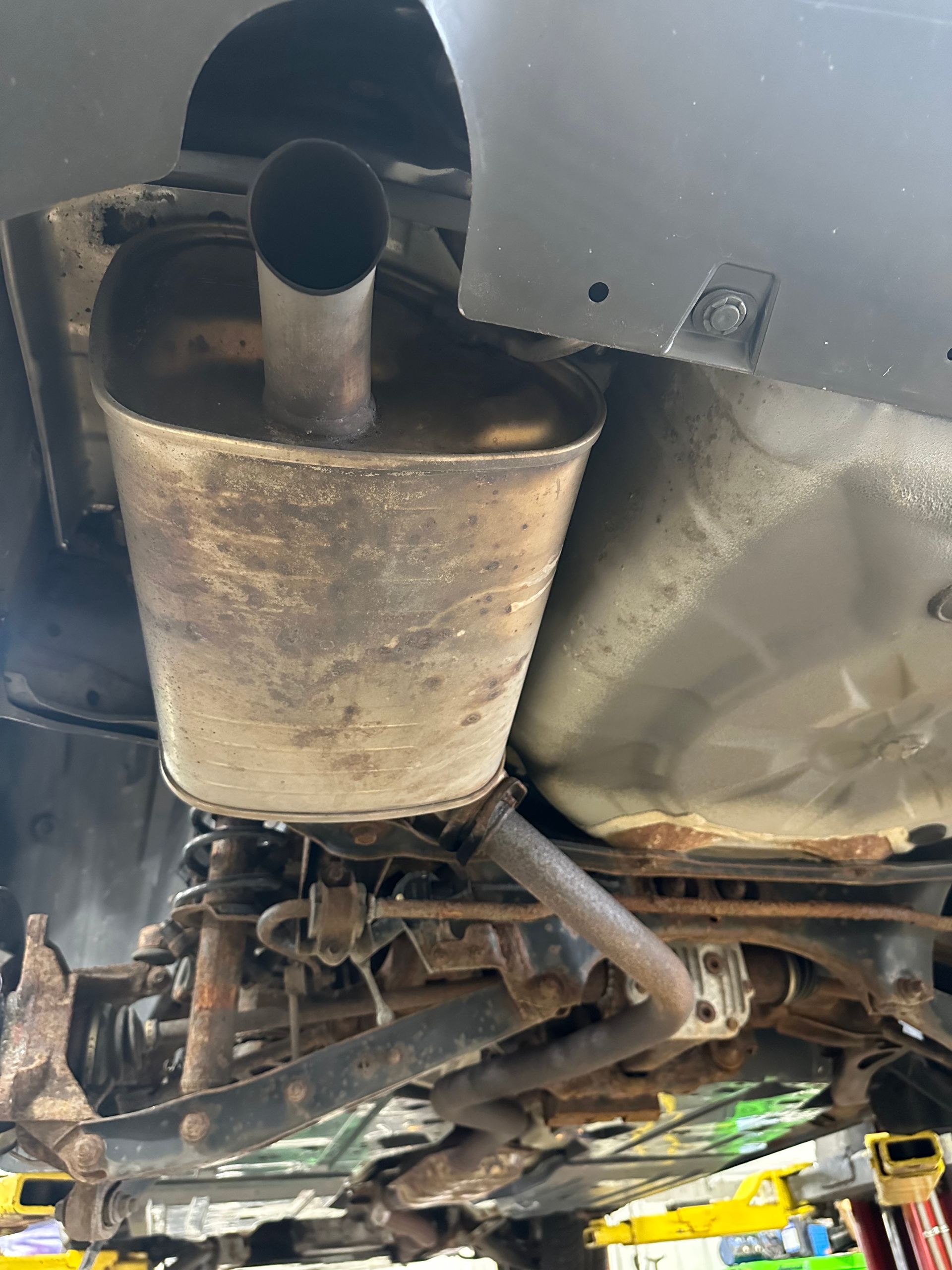 Rusty exhaust system under a grey vehicle in the auto repair shop.